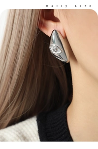 Close-up of teardrop stud earring featuring an embossed evil eye design with a crystal