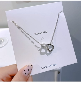 Close-up of silver dual-ring heart necklace with diamonds on a Thank You display card