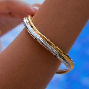 Primo piano di bracciali intrecciati in oro, argento e oro rosa con finitura lucida
