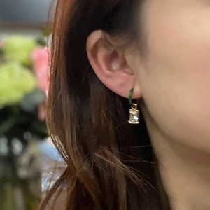 Close-up of gold earring featuring a rectangular zircon pendant worn by a model