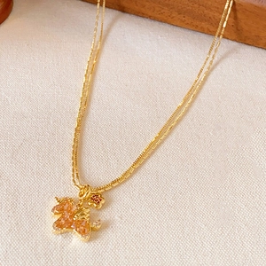 Golden unicorn necklace with orange crystal and flower pendant on beige fabric