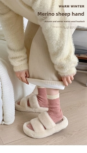 Close-up of pink striped merino wool socks and plush slippers on wooden floor