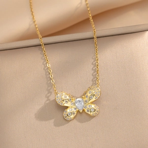 Minimalist gold butterfly necklace with sparkling zircon pendant on a beige background