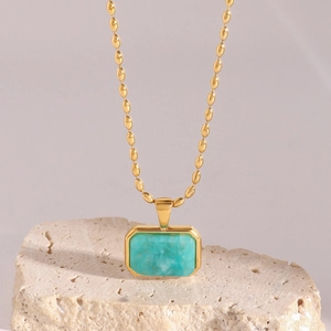 Detail of turquoise pendant necklace with golden beaded chain on a stone display stand