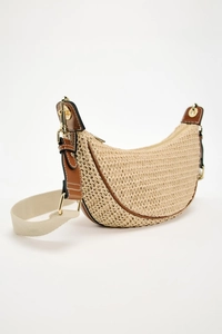 Detail of beige woven crescent bag featuring brown leather trim and golden hardware
