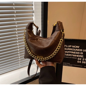 Detail of dark brown pleated leather bag with gold chain strap and zipper closure
