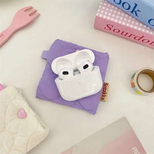 Close-up of quilted purple mini headphone pouch with white wireless earbuds on a desk