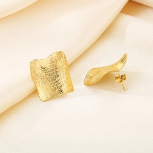 Macro detail of gold irregular square earrings with embossed crocodile pattern texture