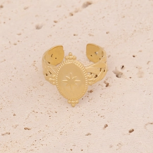 Close-up of gold starburst engraved oval ring on a textured stone surface
