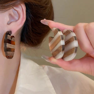 Detail of C-shaped striped earrings featuring brown wood and cream resin textures