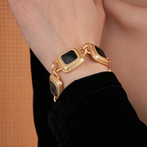 Close-up of a vintage golden bracelet with square black inserts worn on a model's wrist
