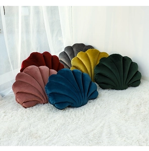 Collection of velvet shell-shaped decorative pillows in various colors on a plush rug