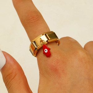 Detailaufnahme des goldenen Modulrings mit rotem Hamsa-Hand-Anhänger am Finger