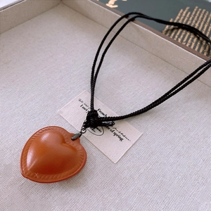 Macro detail of a heart-shaped leather pendant with fine stitching and woven cord strap