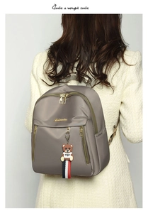 Detail of grey oxford backpack with gold zippers and a cute bear pendant on model back