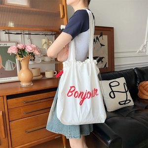 Detail of white canvas drawstring shoulder bag with red Bonjour print on vintage background
