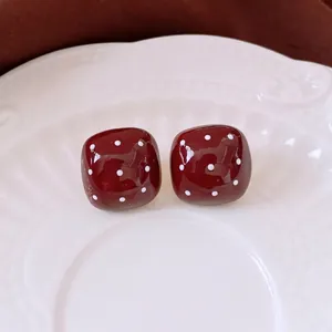 Deep red square earrings with white polka dots on elegant white ceramic plate