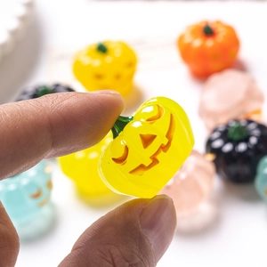 Hand holding a glowing yellow translucent Halloween pumpkin bead with carved smiling face