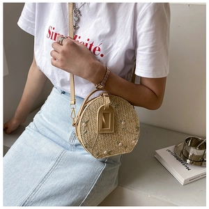 Detail of round straw bag with flower embroidery shown as a crossbody on a model