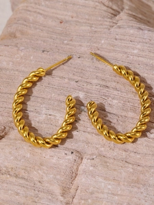 Detailed macro shot of a gold-plated twisted rope geometric C-shaped earring on a stone