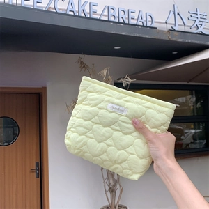 Close-up of cream quilted heart pattern makeup bag with zipper and logo label