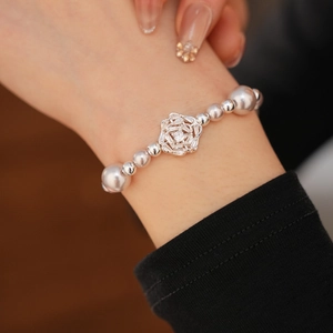 Detailed view of zircon flower pearl bracelet worn on a woman's wrist with silver beads