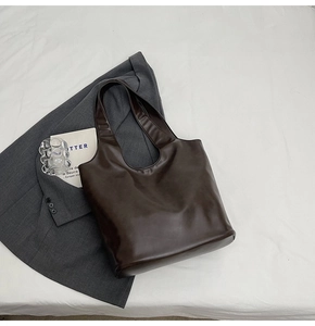 Flat lay of a large dark brown PU leather tote bag on white fabric with a grey blazer