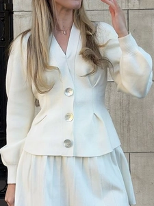 Detailed view of white V-neck knit cardigan with shell buttons and pleated skirt texture