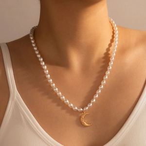 Detail view of pearl necklace with gold crescent moon pendant worn on collarbone