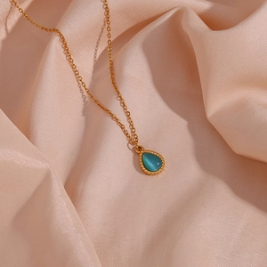 Macro detail of gold teardrop necklace with cat-eye stone on pink satin fabric