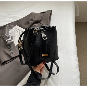 Detail view of a black lychee texture bucket bag with gold hardware on white bedding