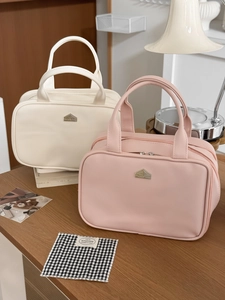 Duo of beige and pink PU leather cosmetic bags with house-shaped metal logo on desk