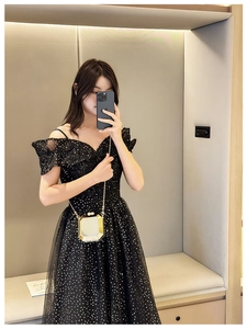Close-up of golden square mirror clutch bag with chain strap held by model in black dress