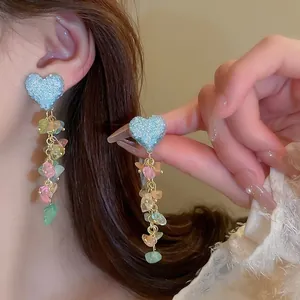 Detail of long tassel earrings featuring blue glitter hearts and colorful stones