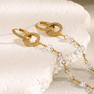 Detail of 18K gold-plated tassel earrings with clear beads on a white stone background