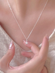 Detail of a minimalist 925 sterling silver star pendant necklace worn on a beige sweater