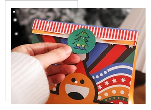 Detail of applying a green Christmas tree sticker to seal festive paper gift bags