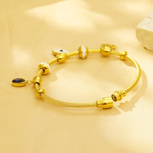 Golden steel cable bracelet with evil eye charms and rhinestone beads on warm background