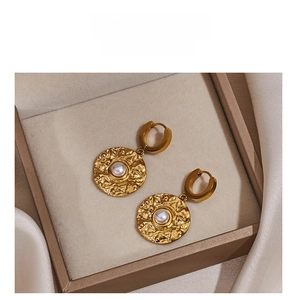 Detailed close-up of gold hammer-textured earrings with pearls on beige silk fabric
