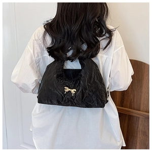 Close-up of black pleated crossbody bag featuring a golden bow detail on textured fabric