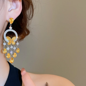 Detail of yellow crystal butterfly tassel earrings worn by a model in soft natural light