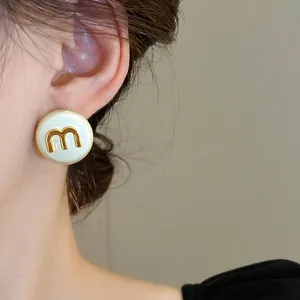 French style creamy round stud earrings featuring a golden letter M metal emblem