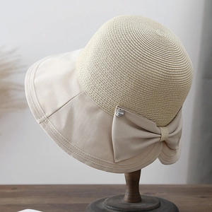 Beige straw and fabric sun hat with large bow on a vintage wooden hat stand