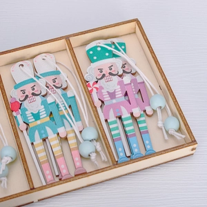 Detail view of 4-piece wooden nutcracker ornaments in pink and cyan in a wooden storage box