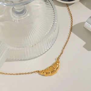 Close-up of golden croissant pendant necklace with delicate polished chain on white background