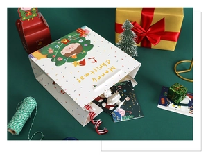 Detailed view of a white Christmas paper gift bag with a cute girl illustration on a green desk
