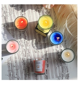 Vista superior de seis velas aromáticas de colores sobre partituras y plumas suaves