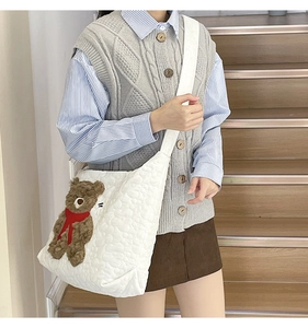 Detailed close-up of a white quilted tote bag with a 3D plush brown bear mascot decoration