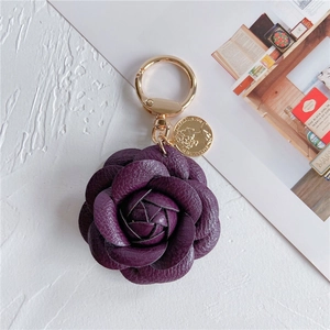 Close-up of a deep purple leather camellia keychain with a gold ring and coin charm