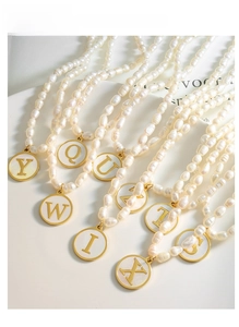 Detail of baroque pearl necklaces featuring gold-rimmed white shell initial pendants